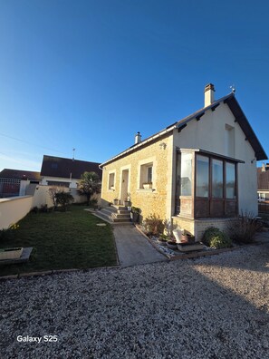 Ein zweistöckiges Haus aus Stein mit geneigtem Dach, einer Veranda und einem kleinen Garten.
