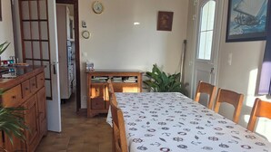 Ein Essbereich mit einem langen Tisch, der mit einer Tischdecke mit maritimen Motiven bedeckt ist, Holzsesseln und einer Holzkommode mit Schubladen.