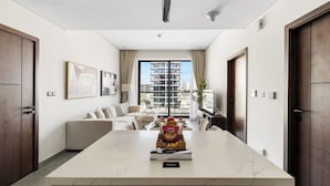 A hotel room with a marble island, a sofa, a dining table, and a view of a building through large windows. - 1BR with Huge Balcony Near Burj Al Arab (Dubai)