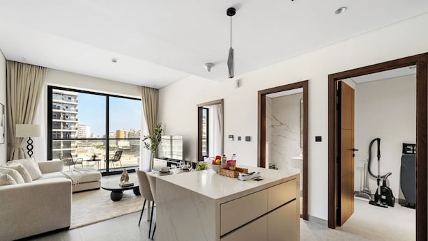 A modern living room with a sofa, a dining table, and a kitchen area with a marble countertop. - 1BR with Huge Balcony Near Burj Al Arab (Dubai)