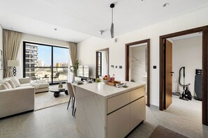 A modern living room with a sofa, a dining table, and a kitchen area with a marble countertop. - 1BR with Huge Balcony Near Burj Al Arab (Dubai)
