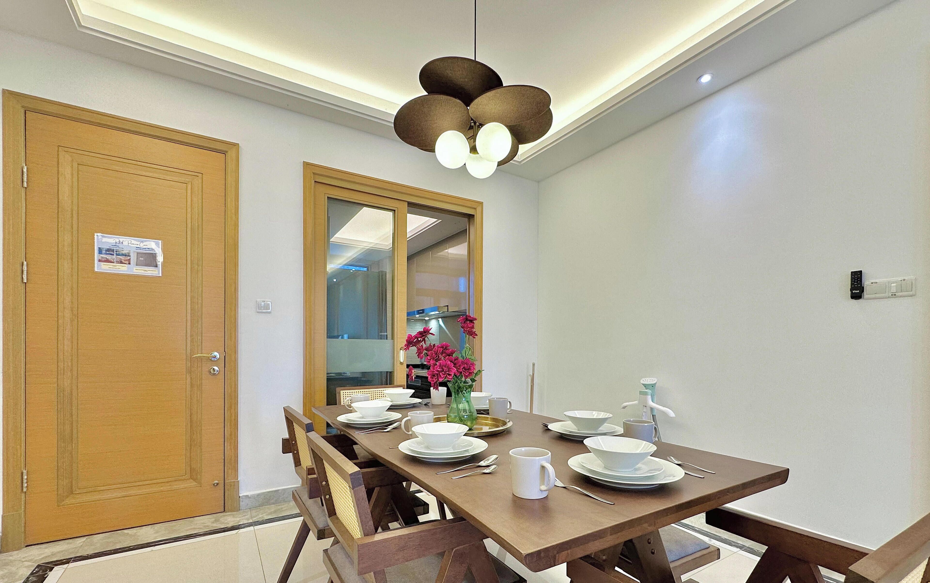 Comedor con una mesa de madera dispuesta para cuatro personas, un ventilador de techo y vistas a otra habitación a través de una puerta de vidrio.