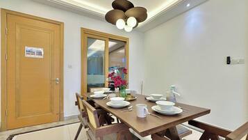 Comedor con una mesa de madera dispuesta para cuatro personas, un ventilador de techo y vistas a otra habitación a través de una puerta de vidrio.