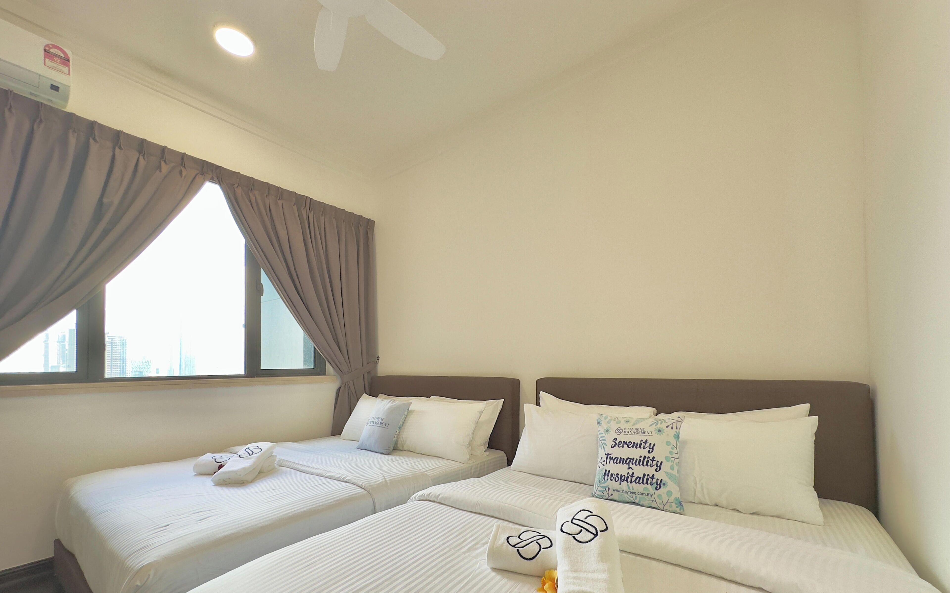 A hotel room with two beds, a window with curtains, a ceiling fan, and a pillow with text.