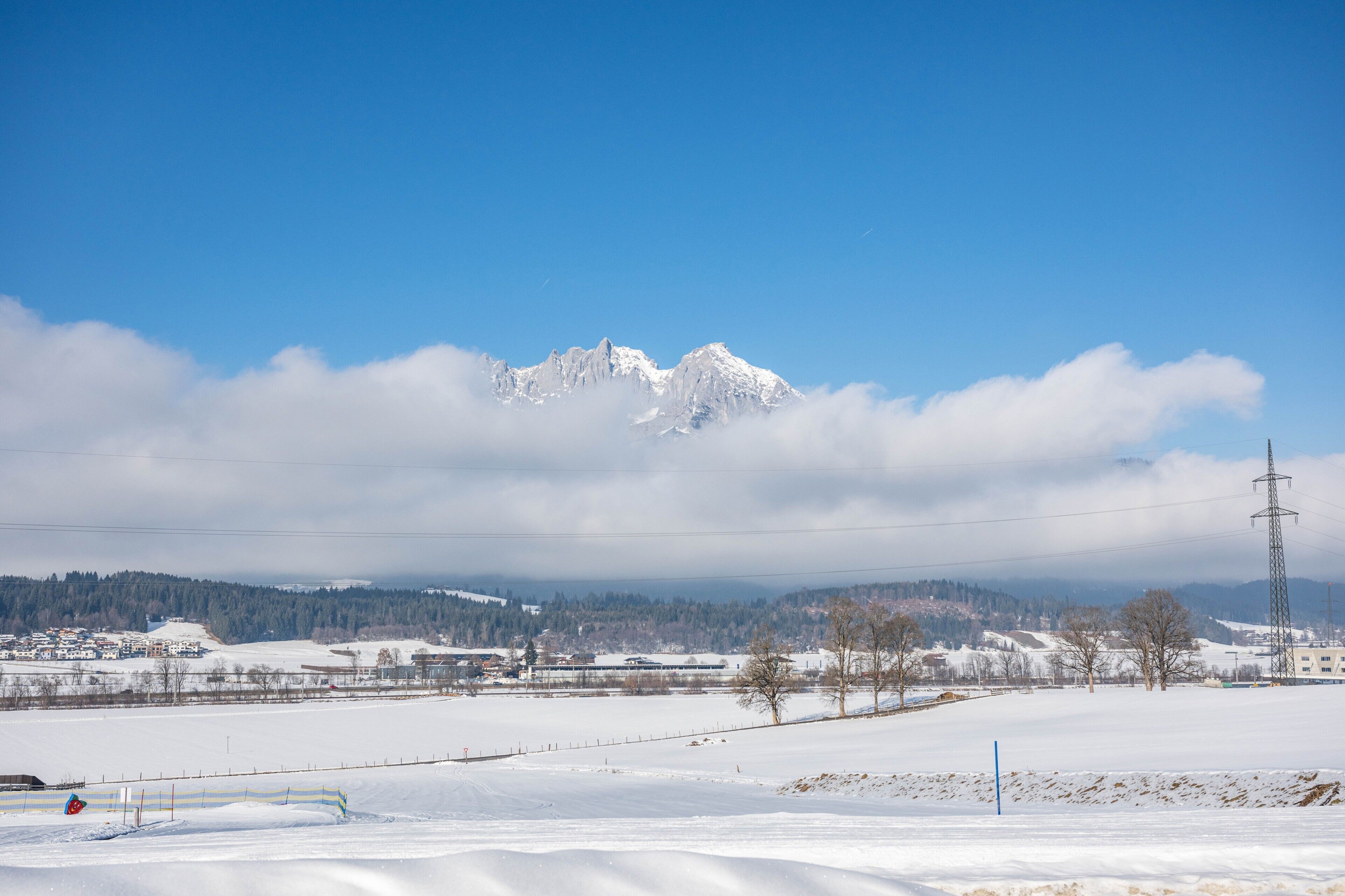 Un paysage enneigé avec une montagne en arrière-plan, une clôture et un pylône de ligne électrique.