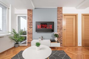 A modern living room with a flat-screen TV mounted on a brick wall, a white console table, a round coffee table, and a potted plant. - Lumina apartment near center of Warsaw (Warszawa BIG)