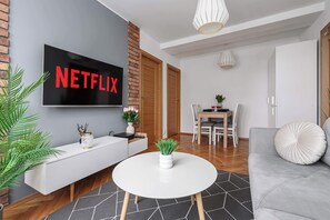 A modern living room with a flat-screen TV displaying the Netflix logo, a white sofa, a round coffee table, and a dining area with a white table and chairs. - Lumina apartment near center of Warsaw (Warszawa BIG)