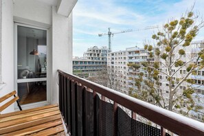 A balcony with a wooden bench, a glass door leading inside, and a view of a construction crane and residential buildings in the background. - Lumina apartment near center of Warsaw (Warszawa BIG)