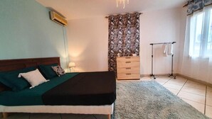A bedroom with a bed, a dresser, a lamp, and a window with curtains. - Ylang Chambres d'Hôtes, Your Villa in Petite Terre, Mayotte (Dzaoudzi Labattoir)