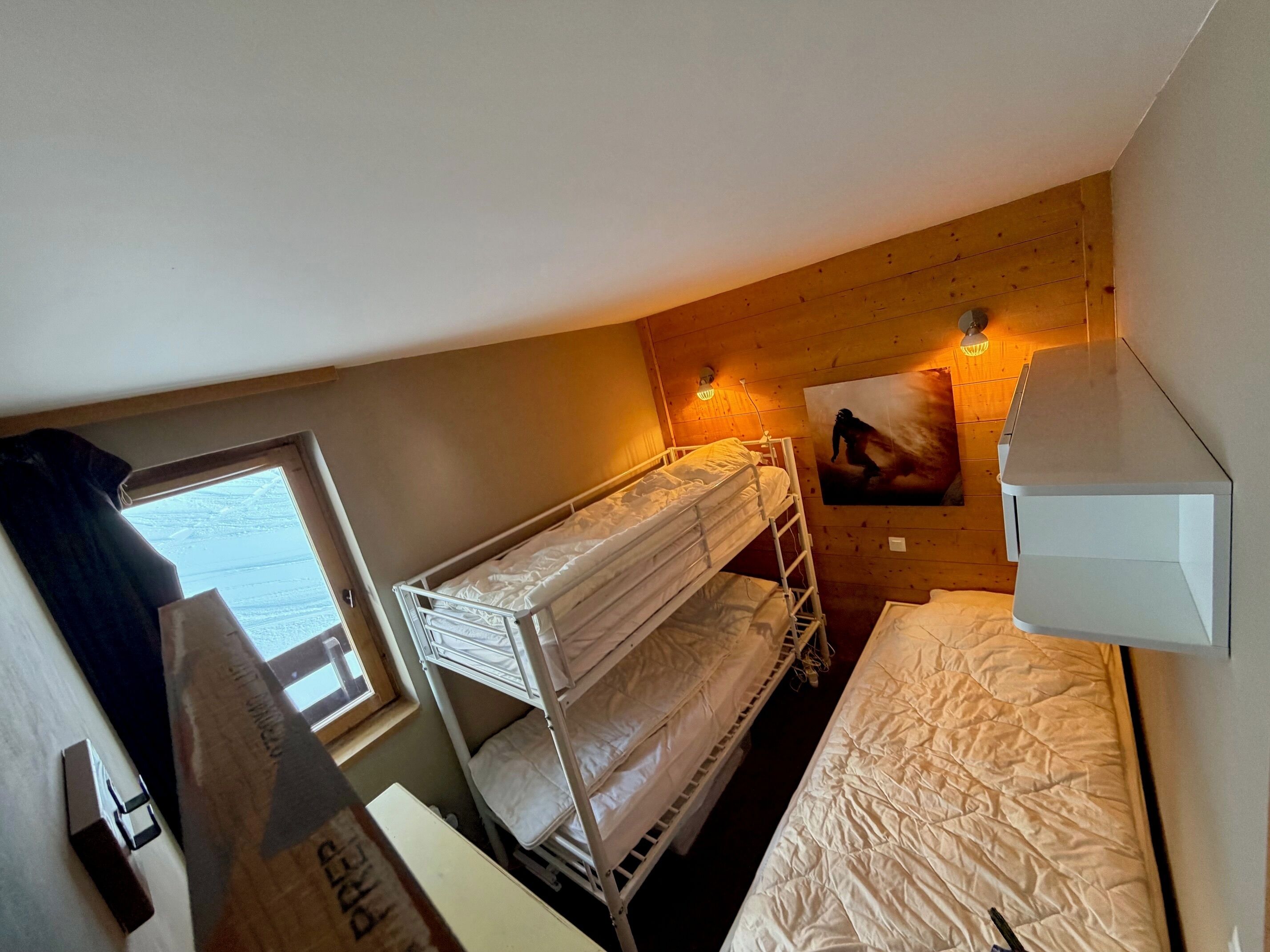 A bunk bed room with a window, a wall-mounted light, and a painting.