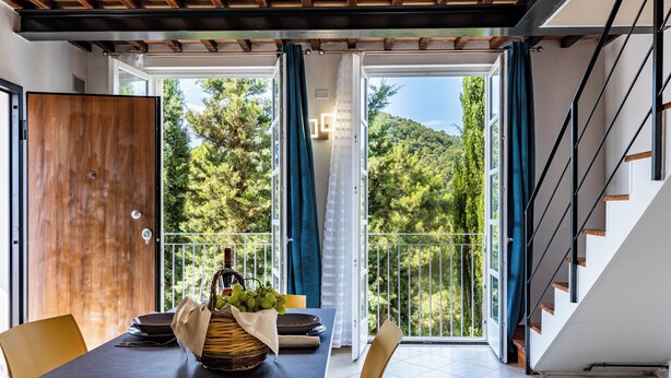 A dining area with a table set for two, a wooden door, and a view of a balcony with a railing and trees. - Giulia Suite with private hot tub (Rivalto Chianni)