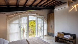 A bedroom with a bed, a bench with towels, a wooden wardrobe, and a large window with curtains. - Giulia Suite with private hot tub (Rivalto Chianni)