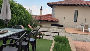A patio with a table and chairs, a small garden area with artificial grass, and a building with a tiled roof. - Disconnect between mountains, with gym, music room and cinema (pets allowed). (MD)