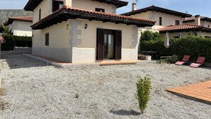 A two-story house with a tiled roof, a small garden area with a gravel path, and a wooden deck with two red lounge chairs. - Disconnect between mountains, with gym, music room and cinema (pets allowed). (MD)