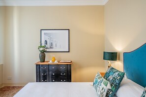 A hotel room with a bed, a dresser, a framed picture on the wall, a lamp, and a decorative pillow. - Operetta Cosy Apartment in Dorsoduro (Venecia)