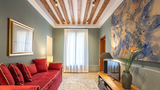 Un saló amb un sofà vermell, un televisor de pantalla plana, un quadre i un ram de flors.