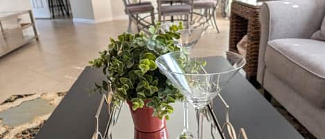 A modern living room with a glass coffee table, a potted plant, and a wine glass.