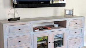 Ein heller Holz-TV-Schrank mit mehreren Schubladen und einer eingebauten Ablage, darüber montiert ein Flachbildfernseher, und auf der Ablage ein kleines gerahmtes Bild.