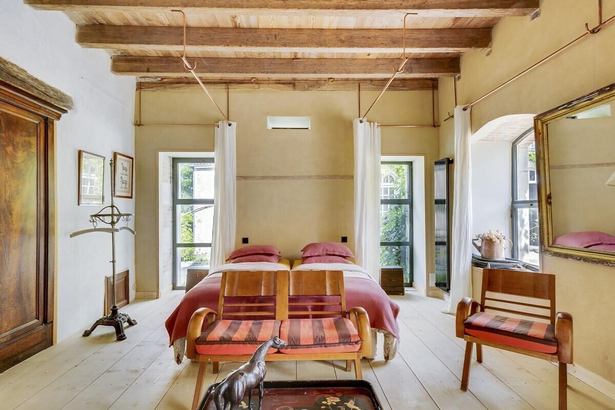 Een kamer met een bed, twee stoelen, een tafeltje en een spiegel.