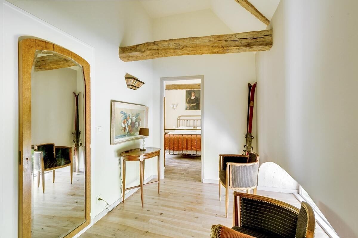 Een ruime kamer met houten balken, een grote spiegel, een schilderij en een bed op de achtergrond.