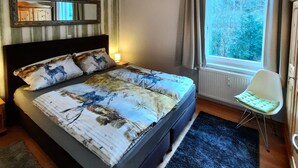 Un dormitorio con una cama grande, una lámpara colgante, una ventana con cortinas y una silla.
