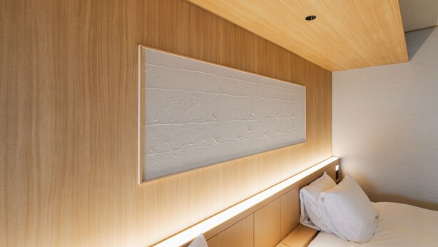Quarto de hotel moderno com cabeceira de madeira, um painel grande fixado na parede e uma luminária de cabeceira.