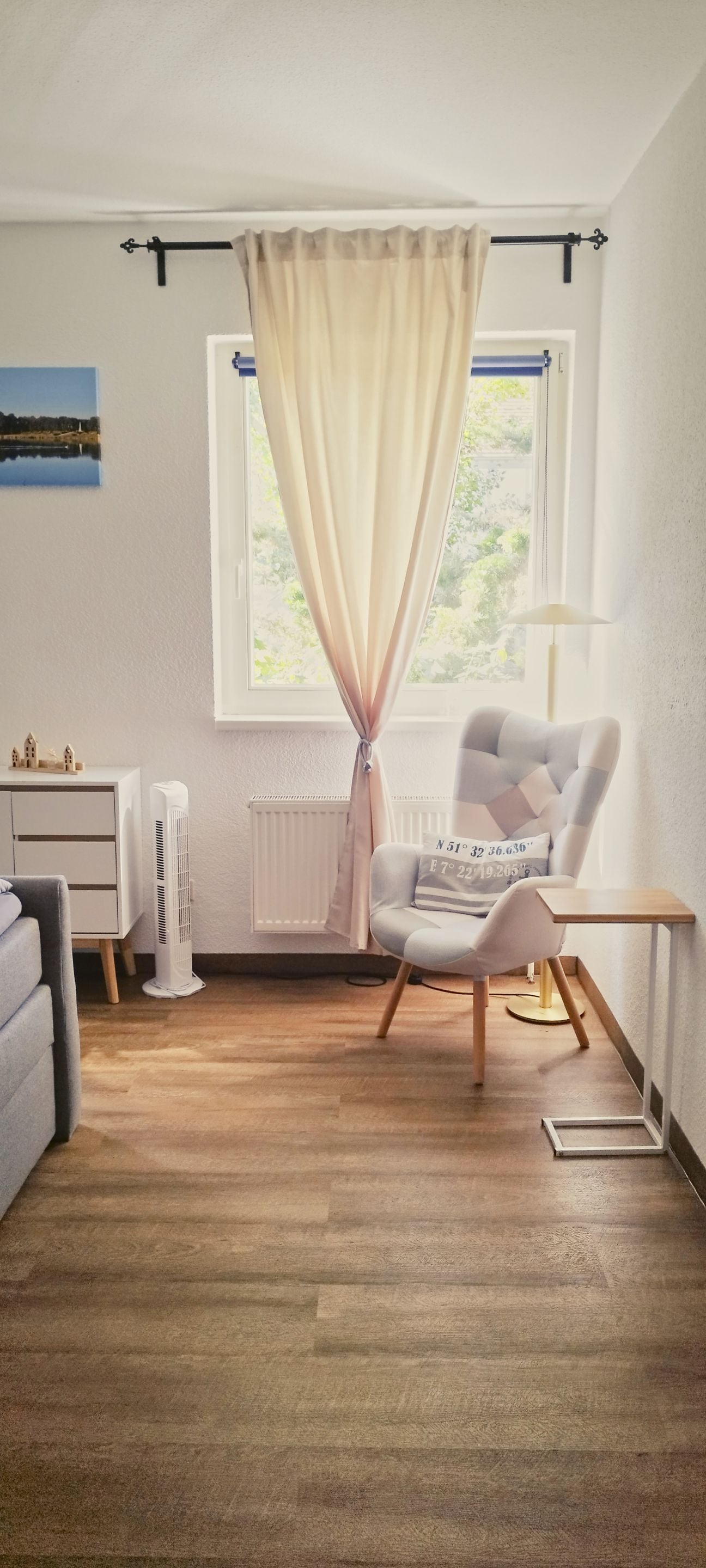A room with a large window, a chair, a desk, a radiator, and a small table.