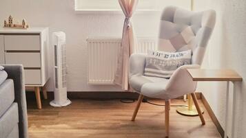 A room with a large window, a chair, a desk, a radiator, and a small table.