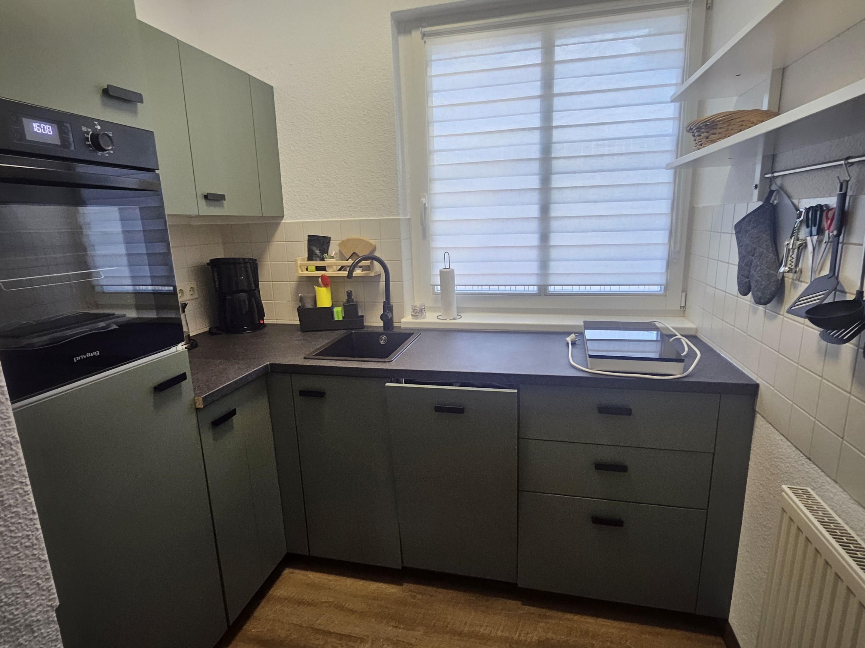Una cocina compacta con horno integrado, un lavamanos y una ventana con persianas.