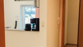 A room with a wooden floor, a kitchen area with a coffee maker, and a door leading to another room.