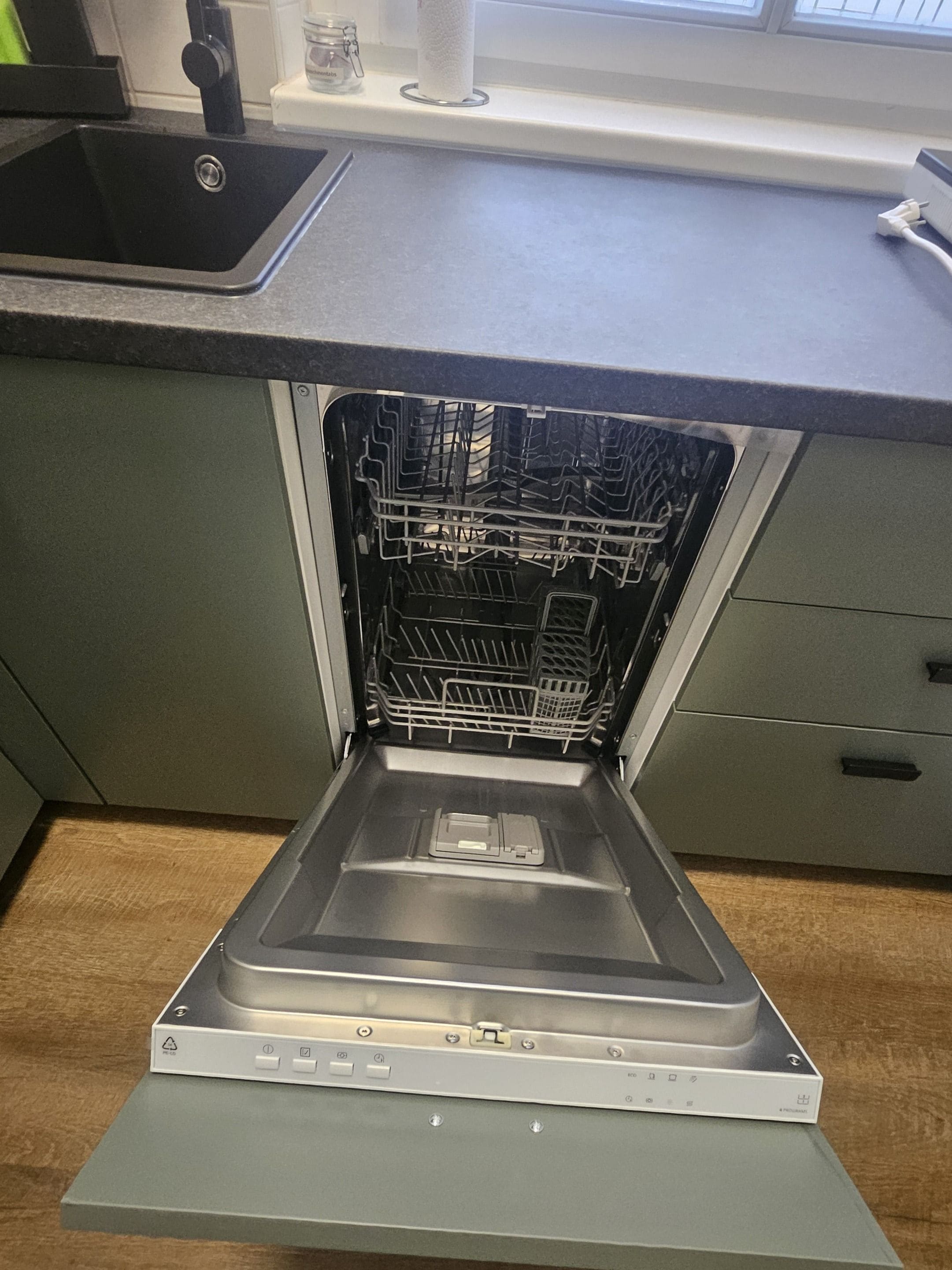 An open dishwasher in a kitchen with a countertop and a window above.