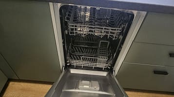 An open dishwasher in a kitchen with a countertop and a window above.