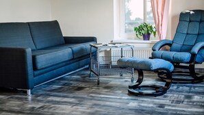 En moderne stue med en mørkeblå sofa, en blå gyngestol og et lille sofabord med en radiator og en potteplante.