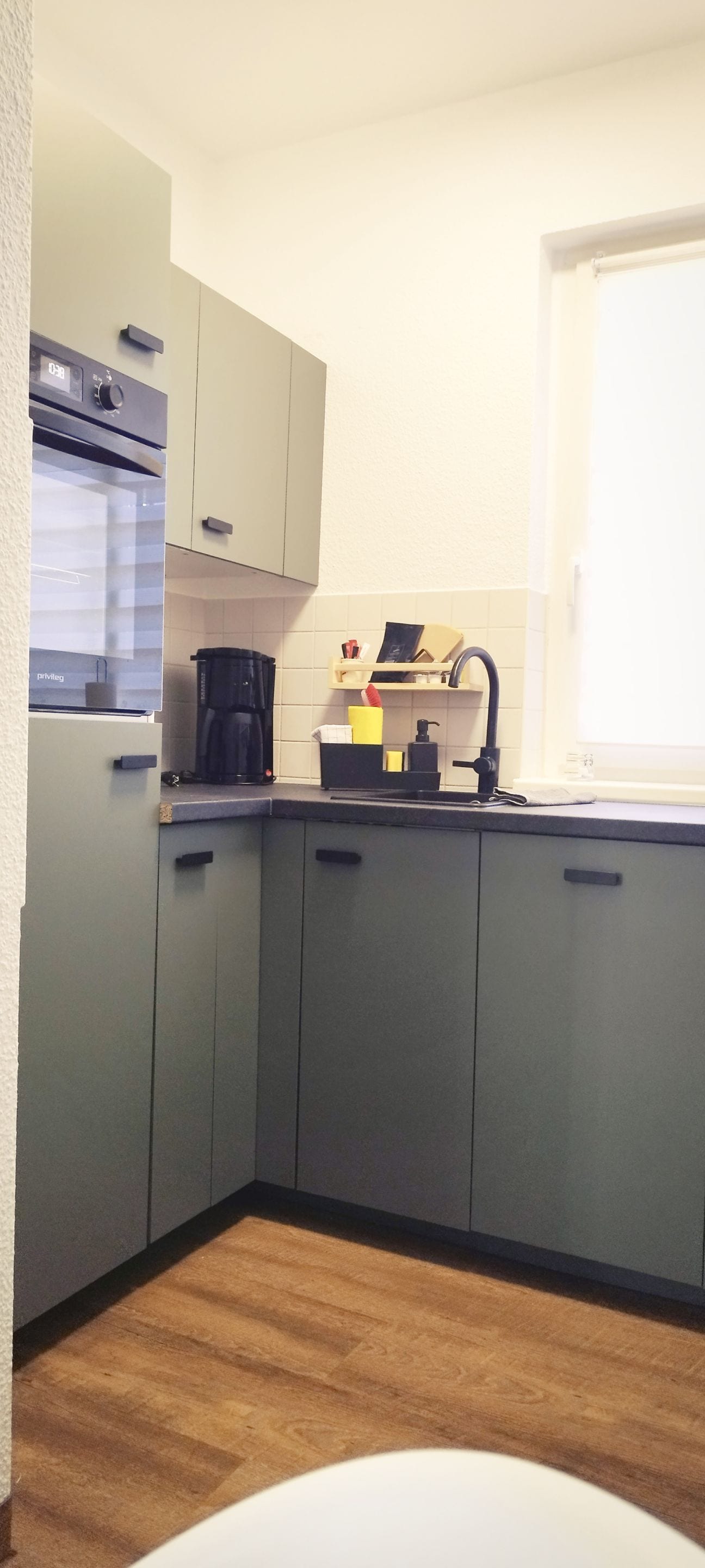 A compact kitchen with grey cabinets, a coffee maker, and a window.