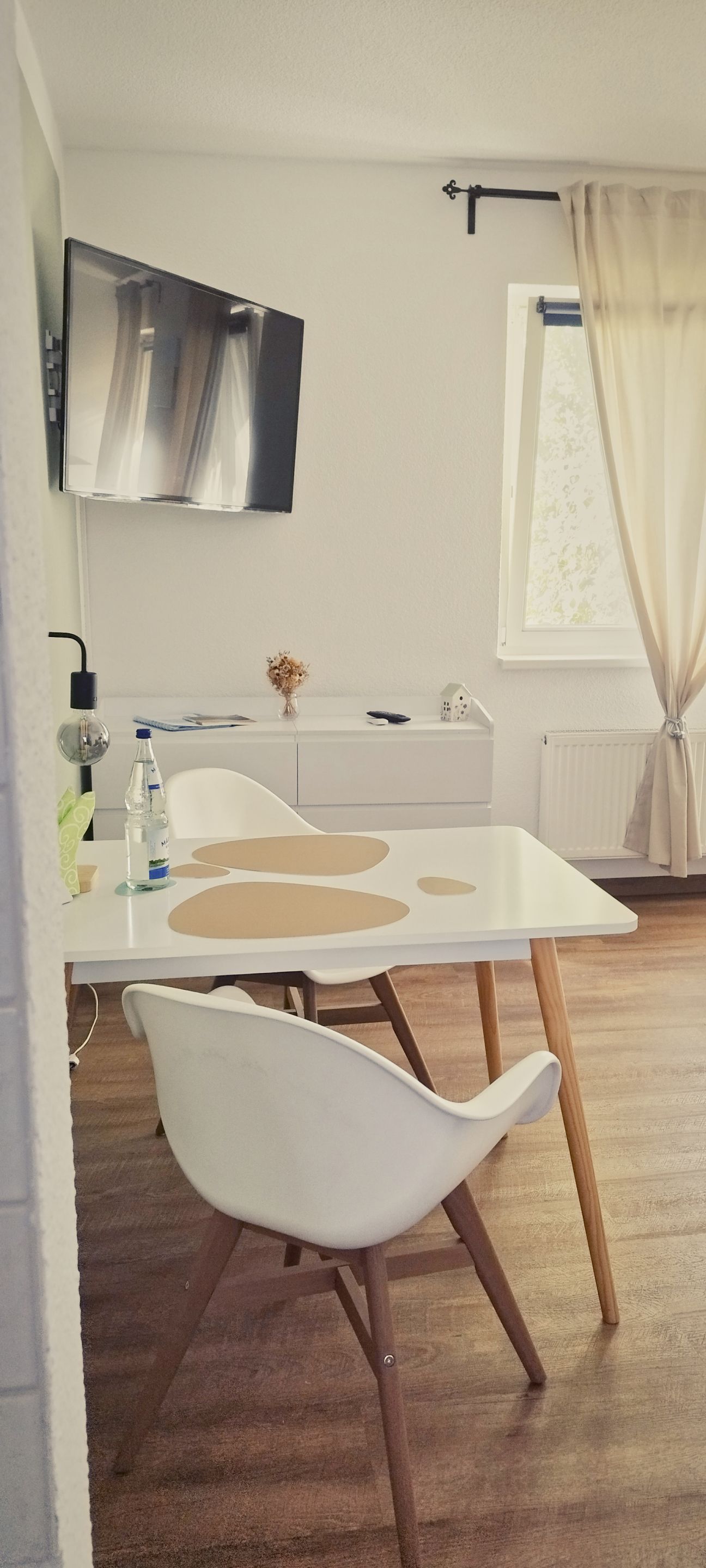 Un comedor moderno con una mesa blanca, una silla blanca, una botella de agua y una pequeña decoración de casa sobre la mesa.