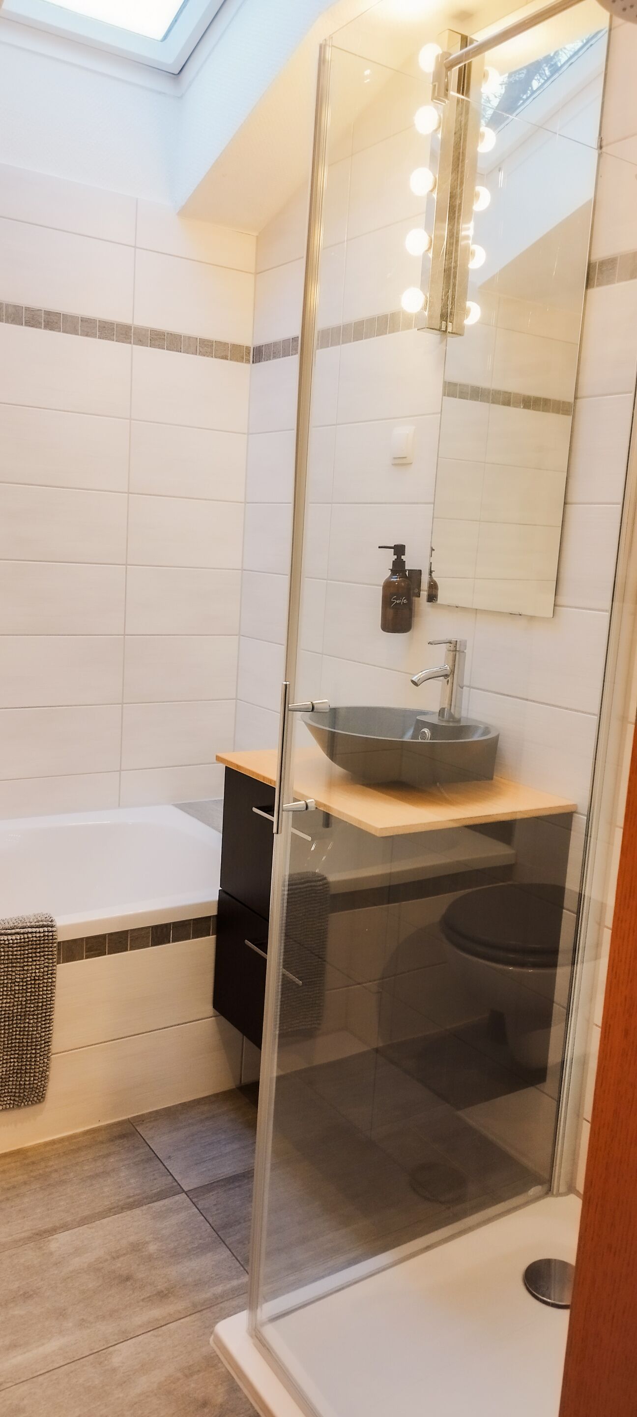 Un baño moderno con cabina de ducha de vidrio, lavamanos sobre encimera y un espejo grande con luces.