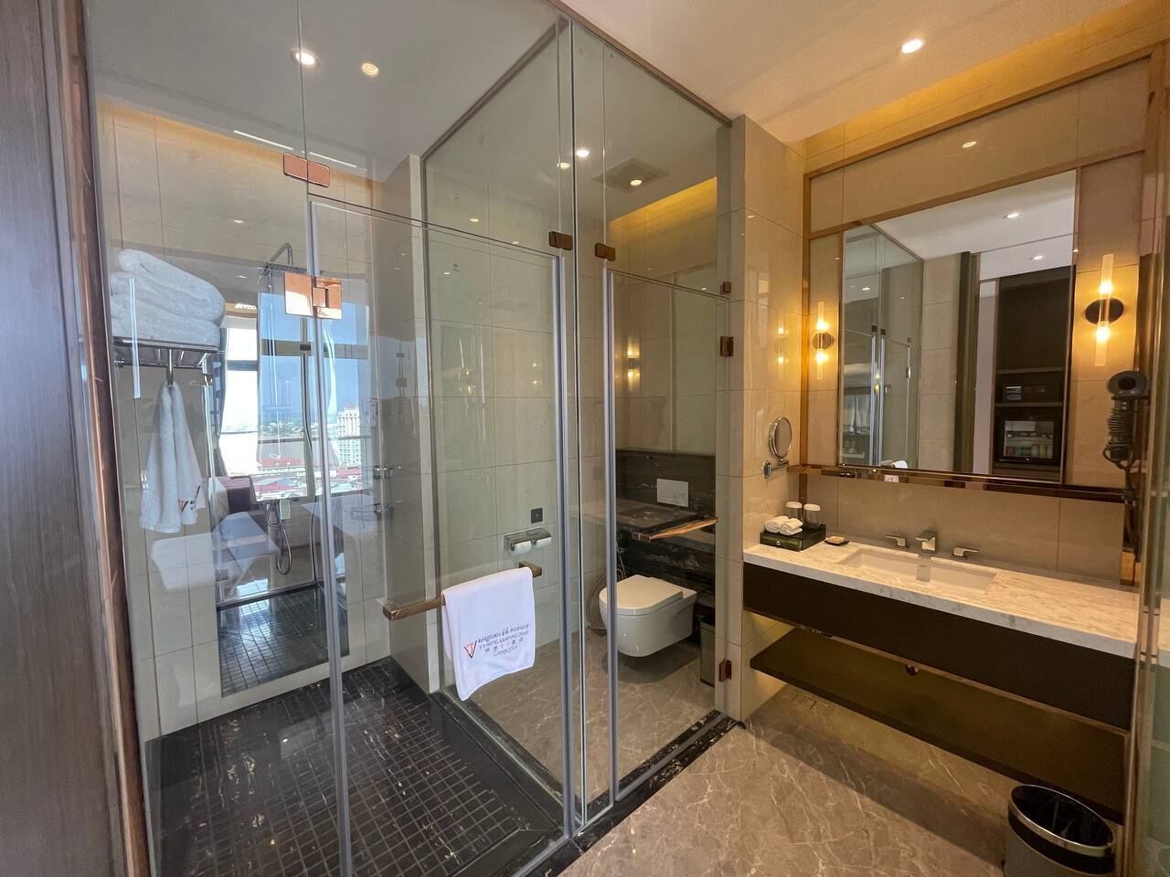 Een moderne badkamer met een douchecabine van glas, een grote spiegel en een marmeren aanrechtblad.
