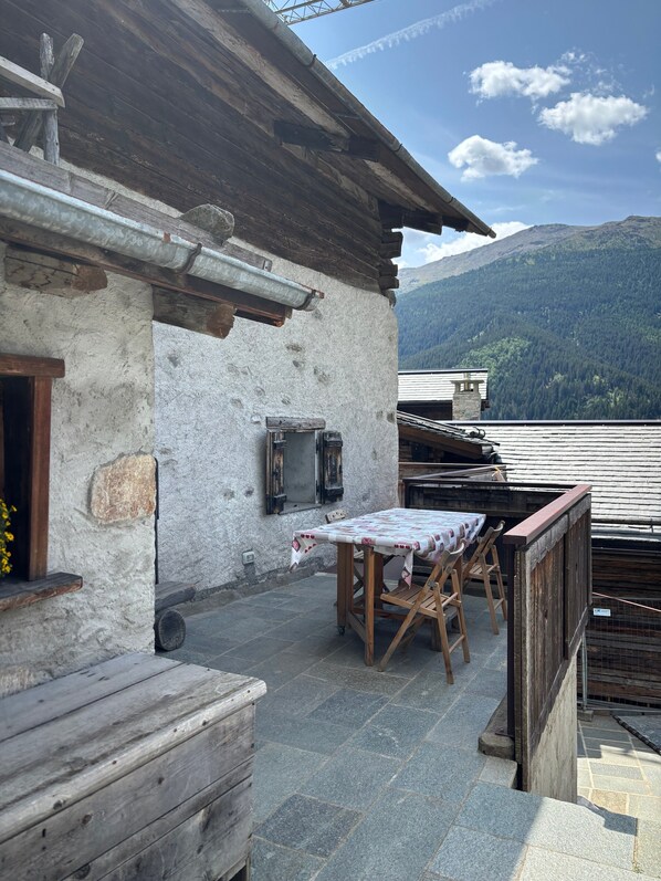 A rustic outdoor seating area with a table and chairs, a wooden bench, and a stone wall.