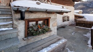 Ein rustikales Steinhaus mit einer hölzernen Bank, einem Fenster mit einem Kranz und Schnee auf dem Dach und dem Boden.