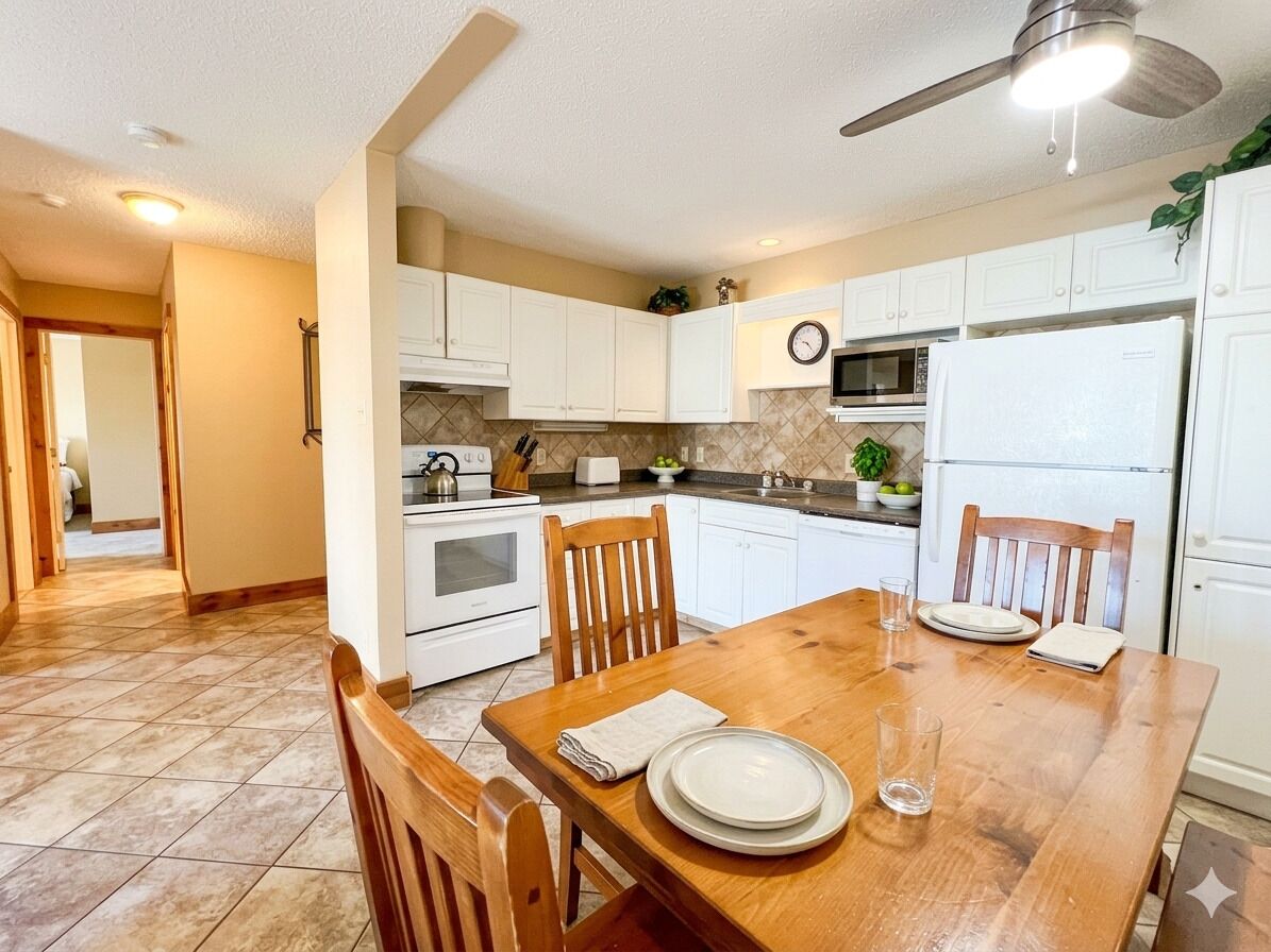Une cuisine avec des meubles blancs, une table à manger en bois et un ventilateur de plafond.