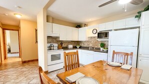 A kitchen with white cabinets, a wooden dining table, and a ceiling fan. - Your clean, comfortable Rocky Mountain escape! True ski-in/ski-out 2BR condo right on the Main Run. Enjoy beautiful views, quality linens, a full kitchen, and year-round hot tub. The perfect, affordable base for family fun and relaxation. (Kimberley)