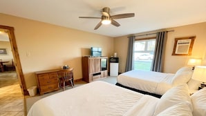 A hotel room with two beds, a desk with a chair, a ceiling fan, a window with curtains, and a view of the outside. - Your clean, comfortable Rocky Mountain escape! True ski-in/ski-out 2BR condo right on the Main Run. Enjoy beautiful views, quality linens, a full kitchen, and year-round hot tub. The perfect, affordable base for family fun and relaxation. (Kimberley)