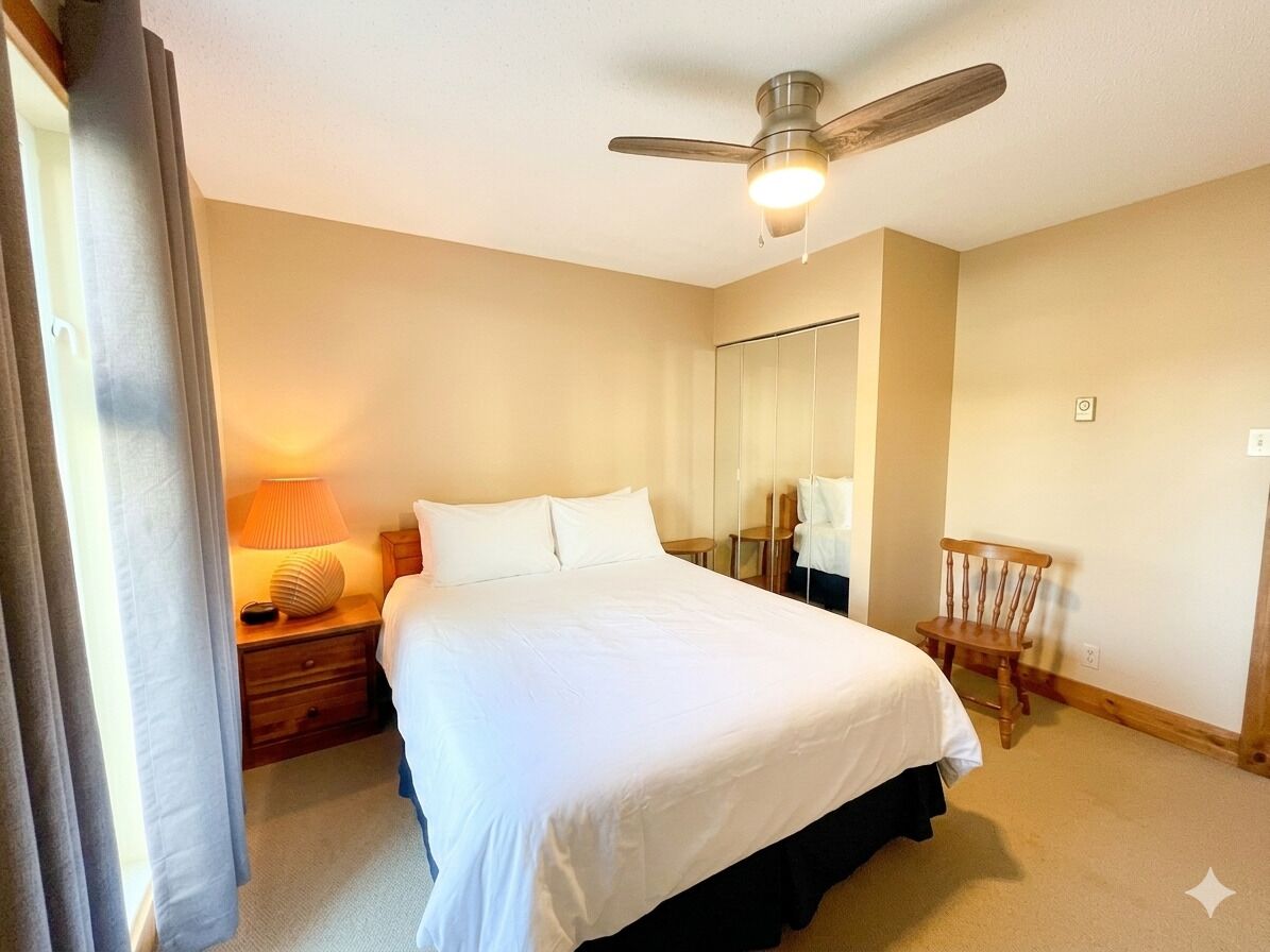 Une chambre d’hôtel avec un lit, une table de chevet, une lampe, un ventilateur de plafond et un miroir.