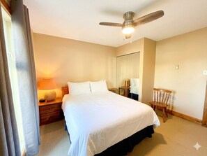 A hotel room with a bed, a nightstand, a lamp, a ceiling fan, and a mirror.