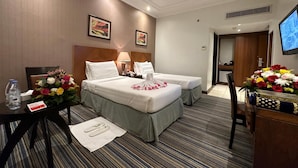Een hotelkamer met twee bedden, een bureau met stoel, een televisie en een bloemenarrangement.