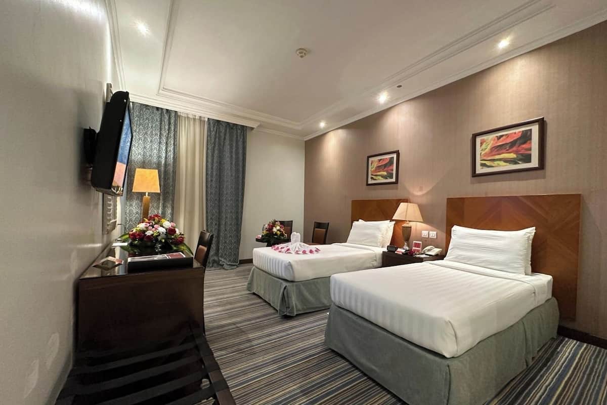 A hotel room with two beds, a desk with a chair, a TV, and two paintings on the wall.