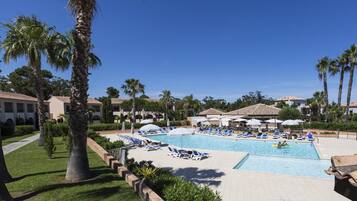 A pool area with lounge chairs and umbrellas, surrounded by palm trees and buildings.