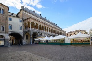 A courtyard with a historic building featuring arches and a covered area with market stalls. - GuestHost - Piazza della Frutta Studio Apartment 1 (Padua)