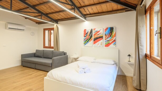 A bedroom with a bed, a gray sofa, and abstract art on the wall. - GuestHost - Piazza della Frutta Studio Apartment 1 (Padua)