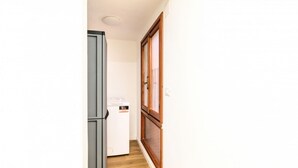 A narrow hallway with a grey refrigerator, a white washing machine, and a wooden door with a window. - GuestHost - Piazza della Frutta Studio Apartment 1 (Padua)